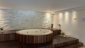 Ett modernt spaområde med ett trädäck, en rund bubbelpool och en stenmur.