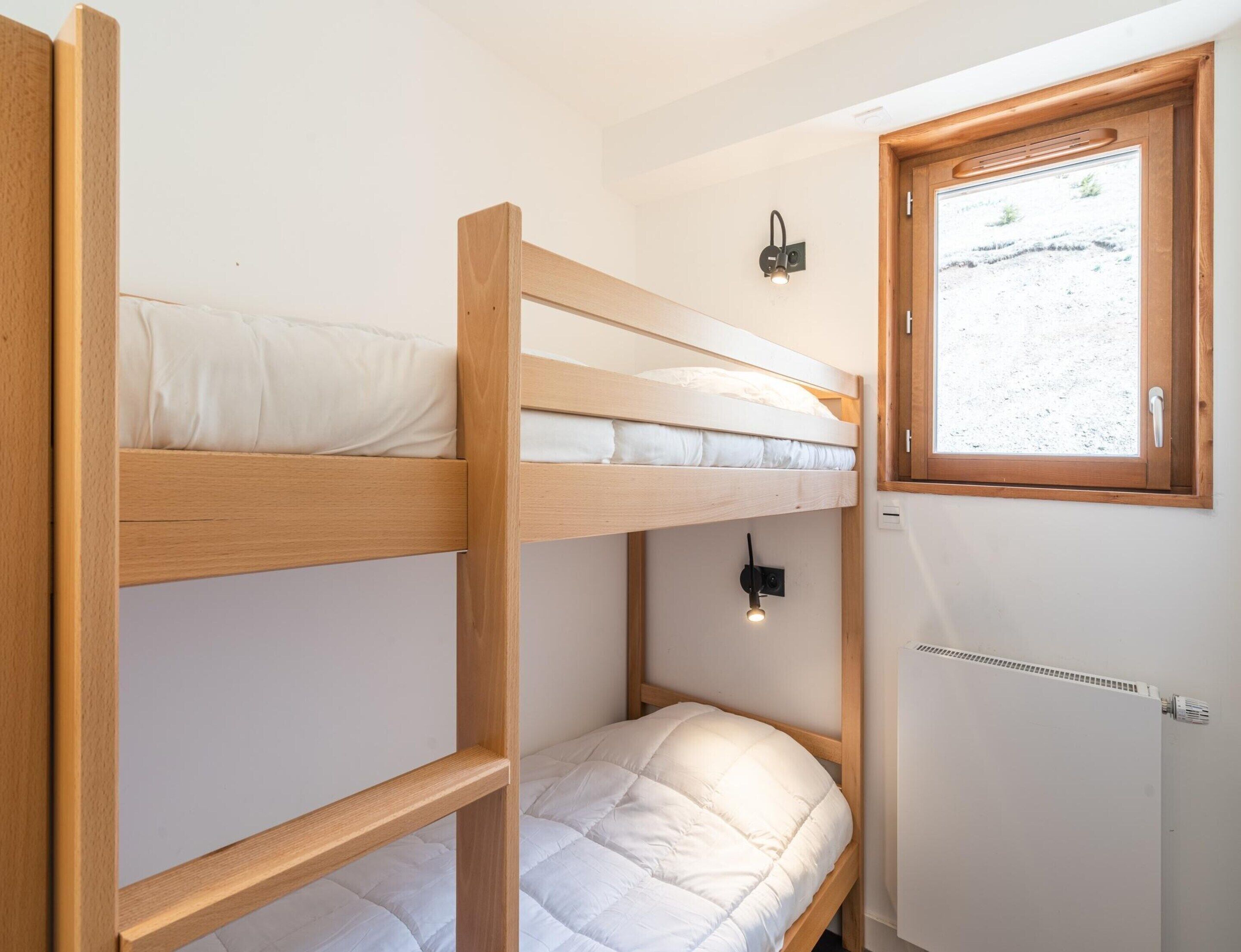 A bunk bed room with a window, a wall-mounted light, and a radiator.