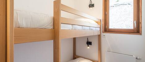 A bunk bed room with a window, a wall-mounted light, and a radiator.