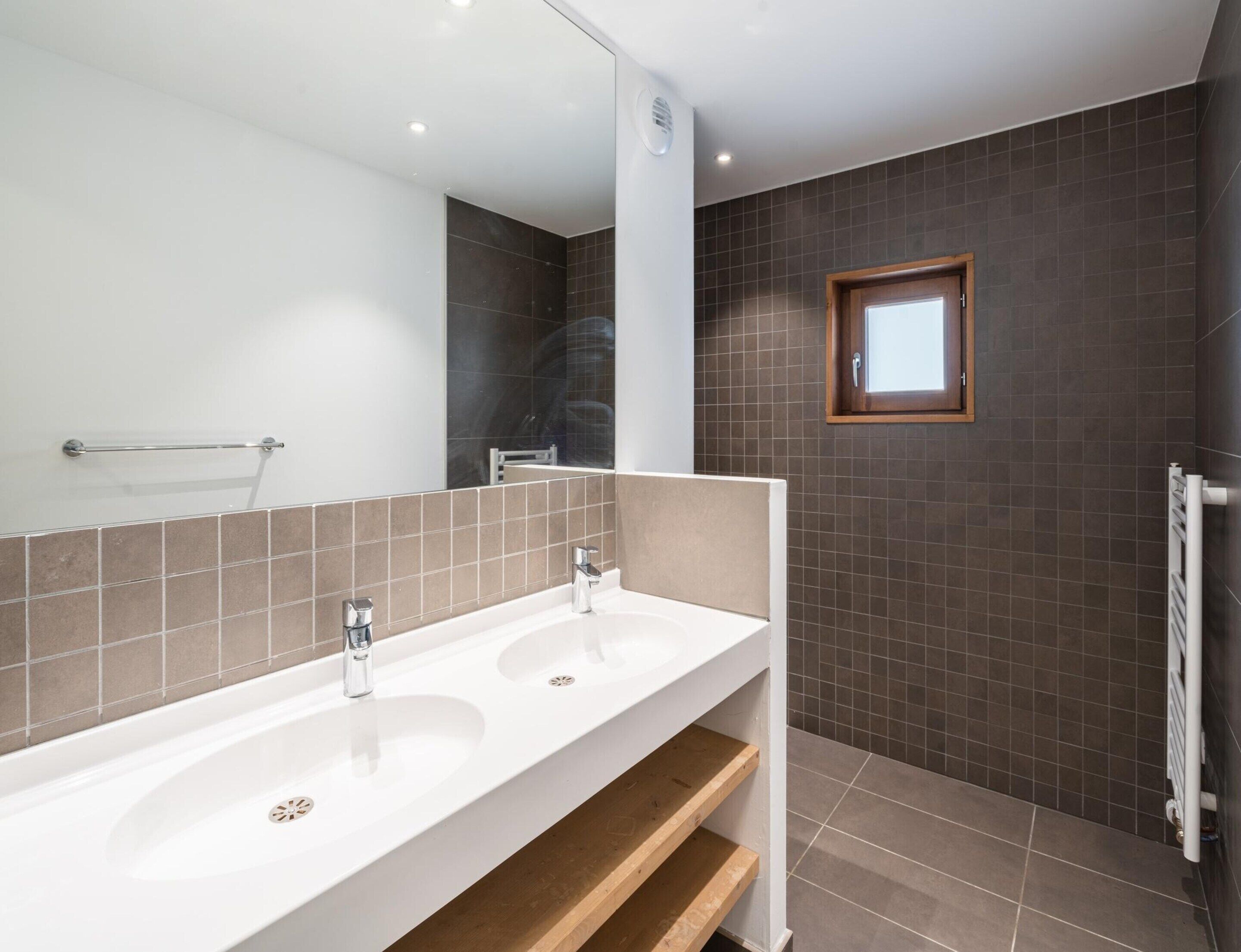 Ein Badezimmer mit zwei Waschbecken, einem Spiegel, einem Fenster und einem Handtuchhalter.
