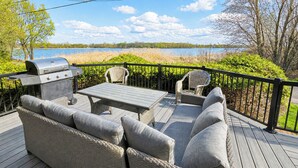 A deck with outdoor furniture, a grill, and a view of a lake.