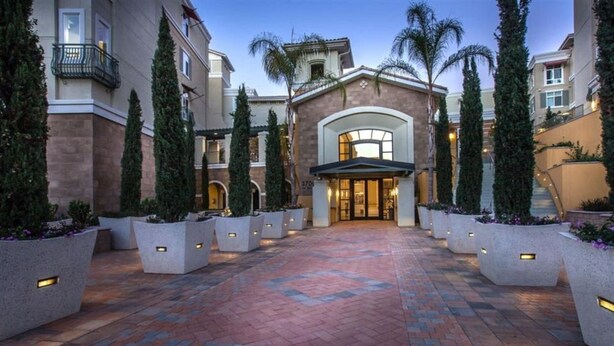 A hotel entrance with a brick pathway, planters, and a building with a large arched entrance. - Elegant Verdant 2BR Retreat with Gym (San Jose)