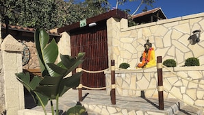 A Buddha statue in a garden area with a stone wall, a wooden fence, and a sign indicating an exit. - House with a Private Pool and Wi-Fi (El Rio)