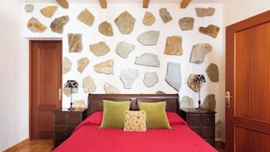 A bedroom with a bed, wooden headboard, a stone wall, and a wooden door. - House with a Private Pool and Wi-Fi (El Rio)