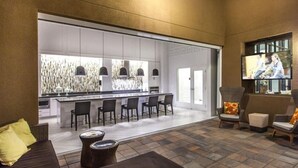 Une cuisine moderne dotée d’un coin bar, de sièges avec des chaises et des poufs, et d’un téléviseur fixé au mur.