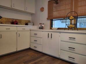 A kitchen with white cabinets, a window with blinds, and a fruit basket on the windowsill.
