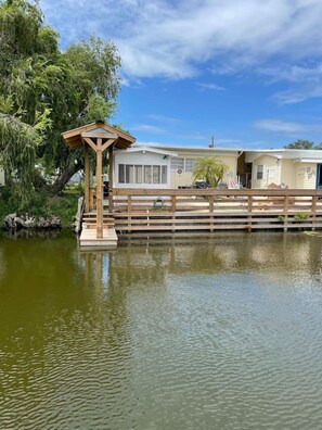 A houseboat with a wooden deck and a small pavilion, surrounded by water and greenery.