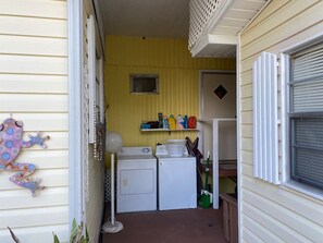 A laundry area with two washing machines, a drying rack, and a shelf with cleaning supplies.