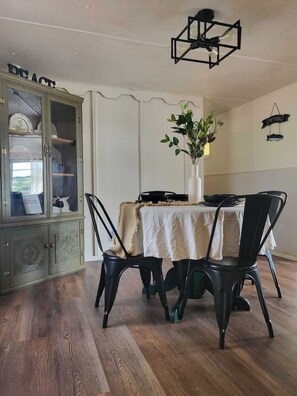 A dining area with a table set for four, surrounded by black chairs, a white tablecloth, and a vase with green plants. A cabinet with glass doors is visible to the left. - Pet Friendly | Private Dock & Direct Canal Access (Okeechobee)