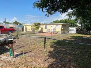 A fenced outdoor area with a yellow building in the background, a red truck, and a metal gate.