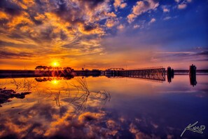 Un tramonto su una superficie d'acqua calma, con un molo che si protende nell'acqua.
