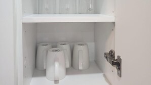 A white cabinet with three clear glass containers on the top shelf and four white mugs on the bottom shelf. - Go-HabitAt: Home away from Home (Saskatoon)