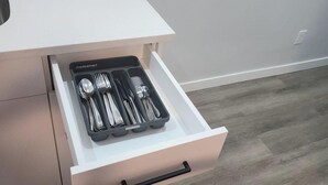 A kitchen with a white countertop, a drawer with utensils, and a grey wooden floor. - Go-HabitAt: Home away from Home (Saskatoon)