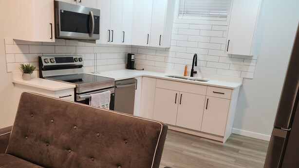 A modern kitchen with white cabinets, a microwave, an oven, and a coffee maker. - Go-HabitAt: Home away from Home (Saskatoon)