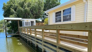 A wooden deck extending over a body of water, leading to a house with a white window and a small porch. - Cottage With Dock | 10 Min To  Lake Okeechobee (Okeechobee)