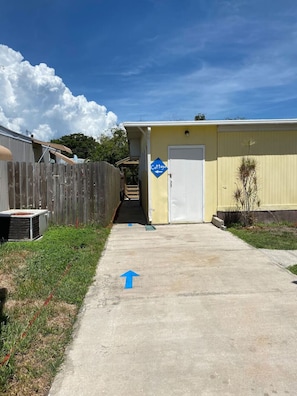 A pathway leading to a building with a 'Cottage' sign, a wooden fence, and a small plant.