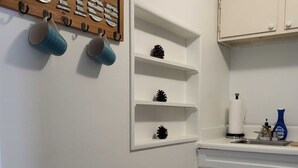 A kitchen with white cabinets, a wooden coffee sign, and a shelf with decorative pinecones. - Cottage With Dock | 10 Min To  Lake Okeechobee (Okeechobee)