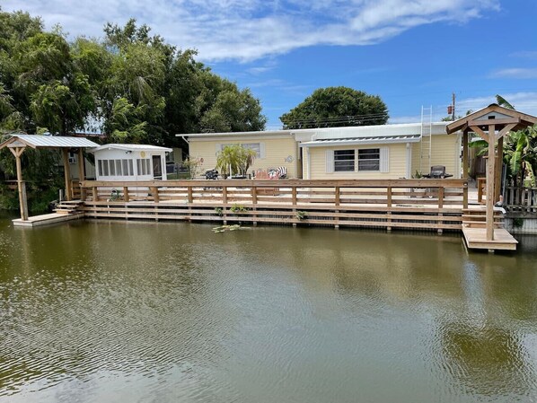 A lakeside property with a wooden deck, a covered seating area, and a small pavilion.