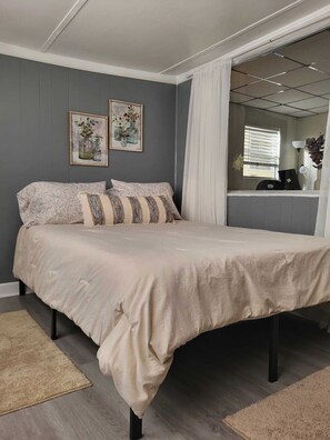 A bedroom with a bed, two framed pictures on the wall, a window with blinds, and a mirror. - Cottage With Dock | 10 Min To  Lake Okeechobee (Okeechobee)