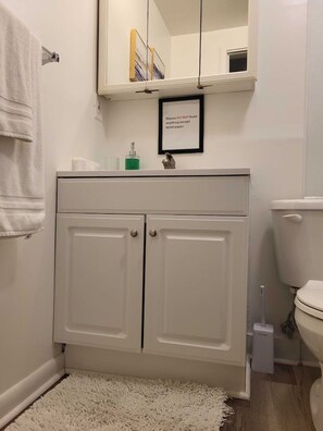 A bathroom with a white sink, two cabinets, a toilet, and a framed sign on the wall. - Cottage With Dock | 10 Min To  Lake Okeechobee (Okeechobee)