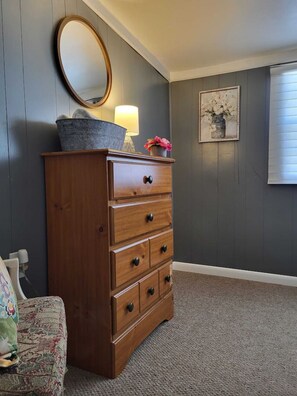 A wooden dresser with drawers, a round mirror, and a lamp on top.