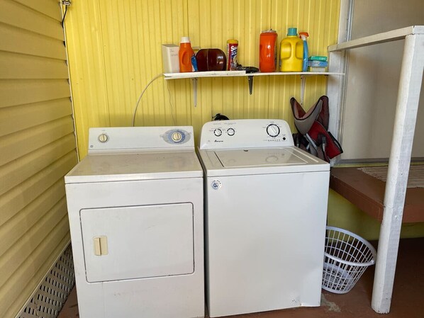 A laundry area with two white washing machines and a shelf above containing various cleaning supplies.