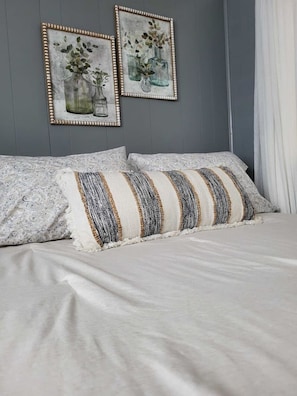 Une chambre à coucher avec un lit, deux tableaux encadrés et une fenêtre avec des rideaux.