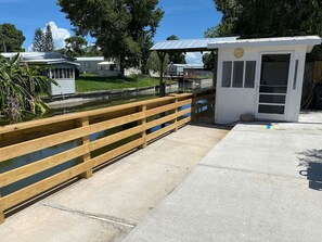 A concrete walkway with a wooden railing leading to a small white building with a clock.