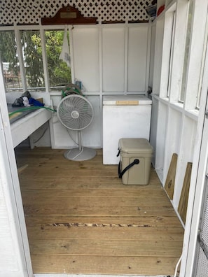 Une petite pièce fermée, dotée d’un plancher en bois, d’un ventilateur blanc, d’une boîte de rangement beige et d’une armoire blanche.