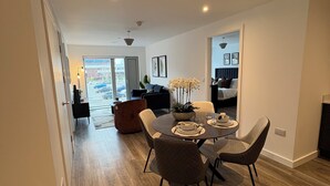 Een moderne woonkamer met een eethoek, houten vloeren en uitzicht door een glazen deur.
