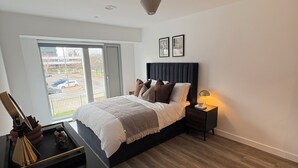 Een slaapkamer met een bed, nachtkastje, lamp en uitzicht.