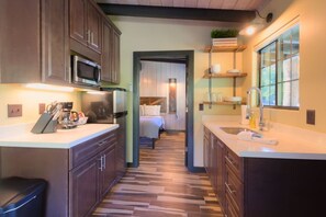 A compact kitchen with a microwave, coffee maker, and a small trash bin. A narrow hallway leads to a bedroom with a bed and a nightstand. - Unit 1 - Slide Rock Lodge (Sedona)