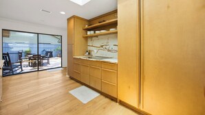 A modern kitchen with wooden cabinets, a marble backsplash, and a sliding glass door leading to an outdoor seating area. - Sea Pines Retreat: Private Deck & Plunge Pool! (Hilton Head Island)