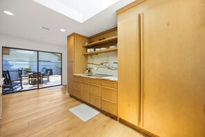 A modern kitchen with wooden cabinets, a marble backsplash, and a sliding glass door leading to an outdoor seating area. - Sea Pines Retreat: Private Deck & Plunge Pool! (Hilton Head Island)