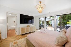 A bedroom with a large bed, a television, a white cabinet, and a sliding glass door leading to an outdoor area. - Sea Pines Retreat: Private Deck & Plunge Pool! (Hilton Head Island)