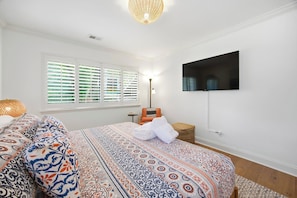 A bedroom with a bed, a television mounted on the wall, a window with blinds, and a bedside lamp. - Sea Pines Retreat: Private Deck & Plunge Pool! (Hilton Head Island)