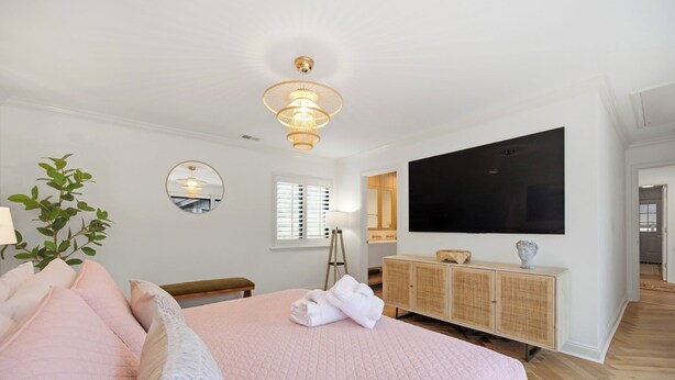 A bedroom with a large bed, a television mounted on the wall, a bedside table, and a mirror. - Sea Pines Retreat: Private Deck & Plunge Pool! (Hilton Head Island)