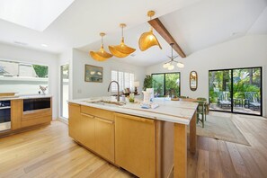 A modern kitchen with wooden cabinets, a large island, and pendant lighting. - Sea Pines Retreat: Private Deck & Plunge Pool! (Hilton Head Island)