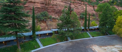 A hotel with multiple guest rooms, a parking area, and a mountainous backdrop.