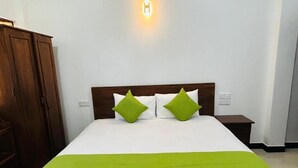 Une chambre d’hôtel avec un lit, deux oreillers verts, une tête de lit en bois, une table de chevet et une lampe fixée au mur.