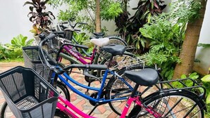 Une rangée de vélos est stationnée dans un espace extérieur agrémenté de plantes en pot et doté d’un sol en briques.