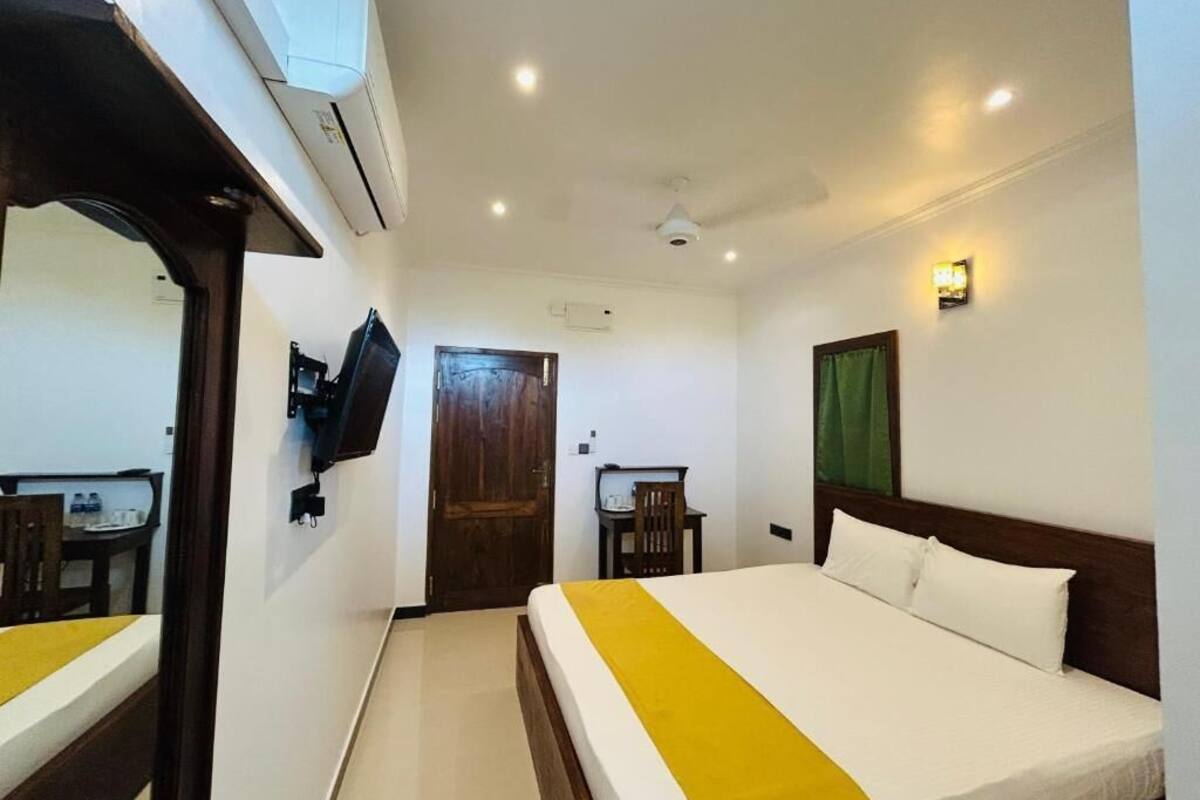 A hotel room with a bed, a desk, a chair, an air conditioning unit, and a television.