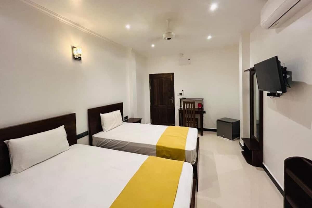 A hotel room with two beds, a television, a desk, and a door.
