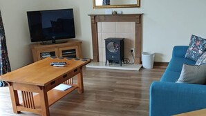A living room with a wooden table, a blue sofa, a television, and a fireplace. - Lovely 3-bedroom house near Robin Hood's Bay perfect for relaxing peaceful break (Robin Hood's Bay)