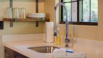 A kitchen with a sink, a faucet, a window, and a shelf with glassware and plates.
