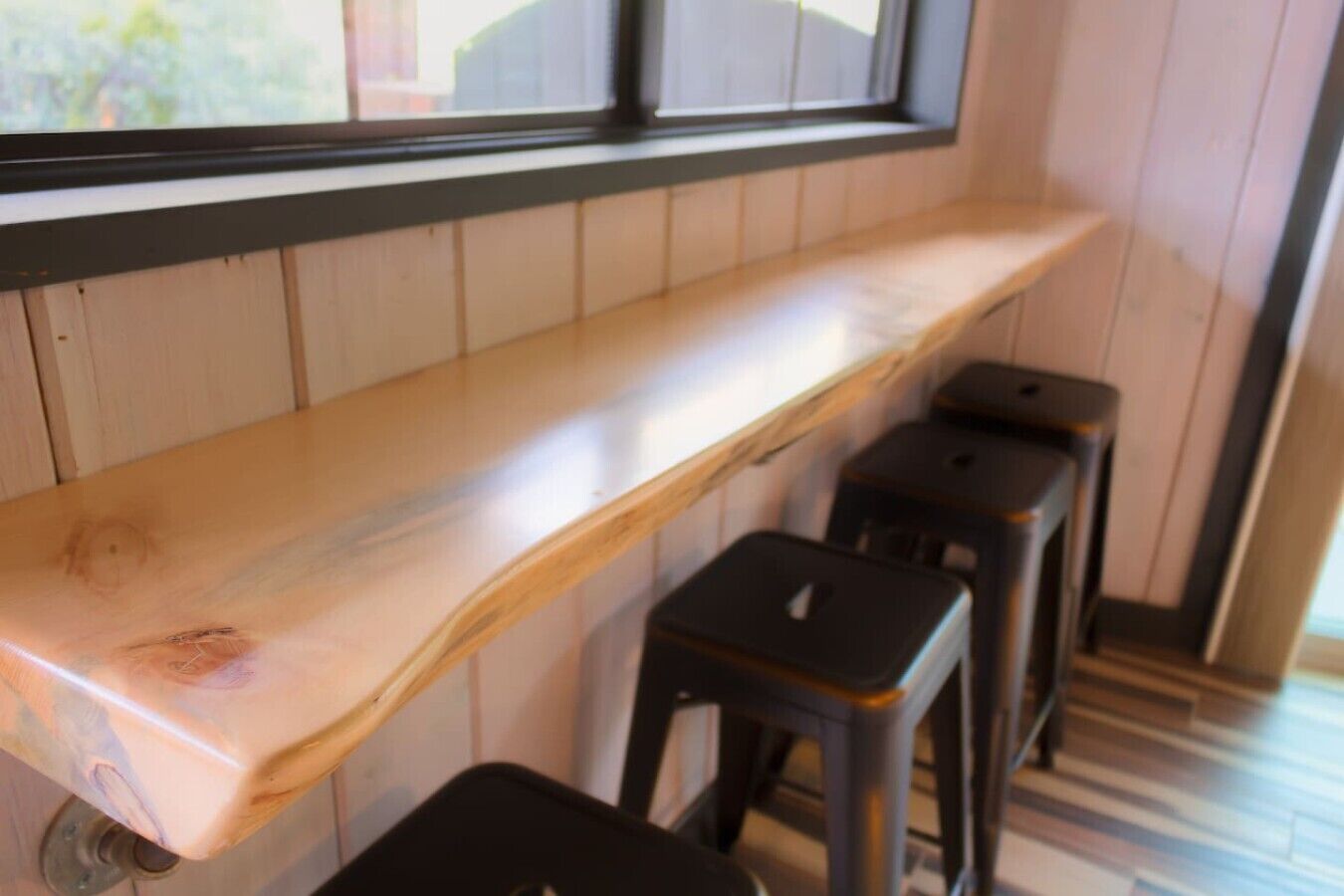 Un banco de madera con un ventanal encima y tres taburetes negros.