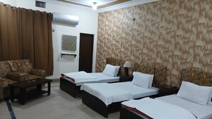 A hotel room with a sofa, two single beds, a small table, an air conditioning unit, and a geometric-patterned wall.