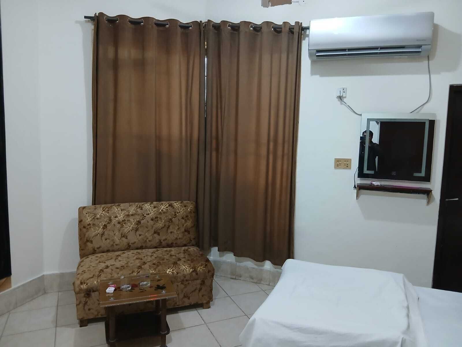 A room with a sofa, a small table, a bed, an air conditioner, and a mirror.