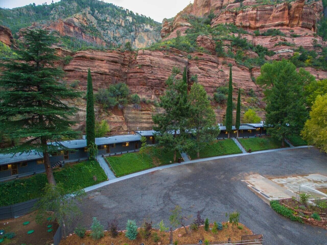 Un hotel con varias habitaciones, un estacionamiento y montañas al fondo.