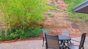 A patio with a table and chairs, surrounded by greenery and a rocky hillside. - Unit 7 - Slide Rock Lodge (Sedona)